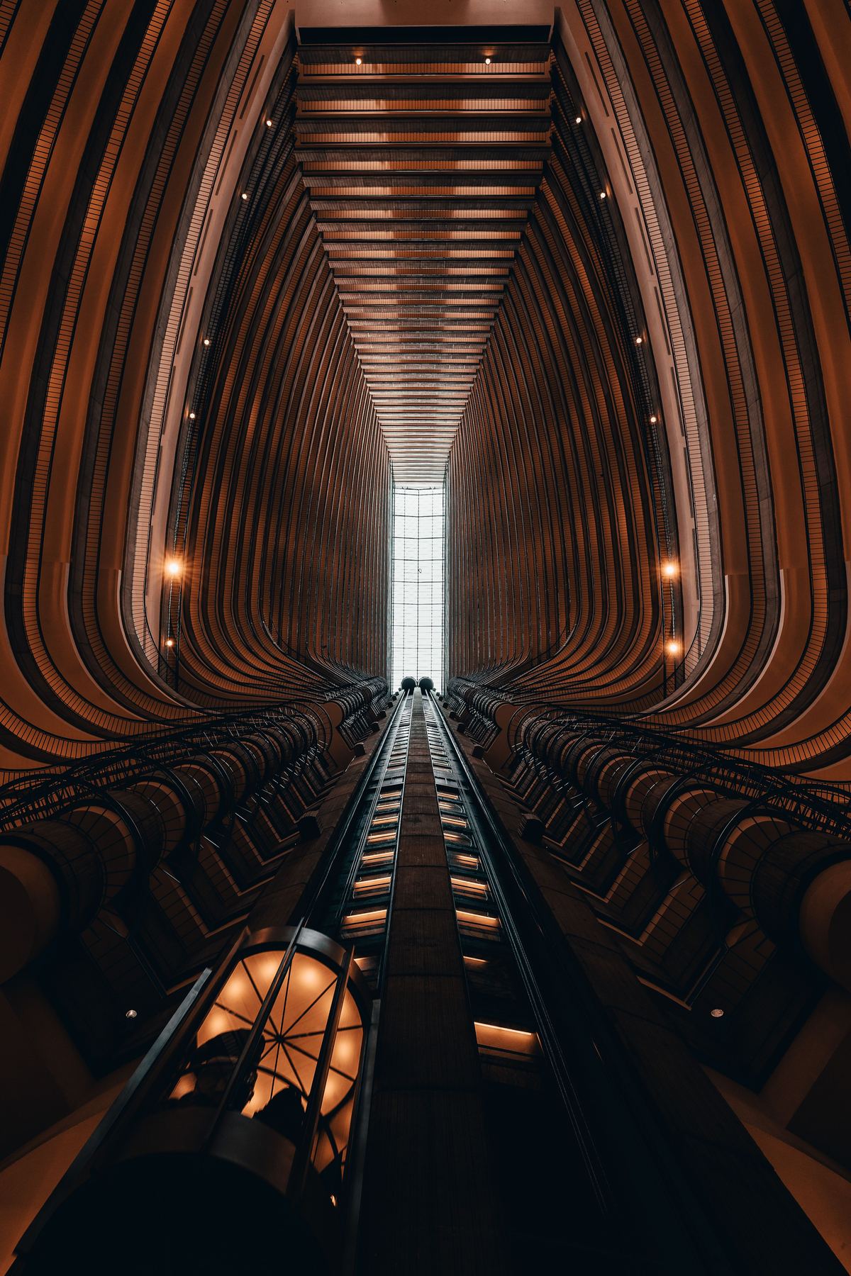 Warm wood-lined elevator atrium viewed from below, tunnel-like perspective toward a skylight