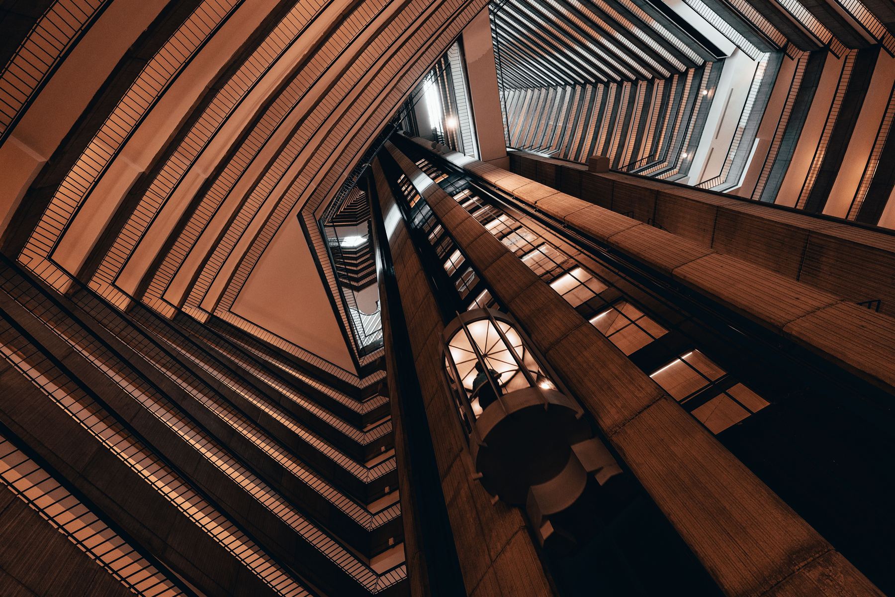 Dramatic upward view of a wood-ribbed elevator atrium with a glass elevator car visible in the center