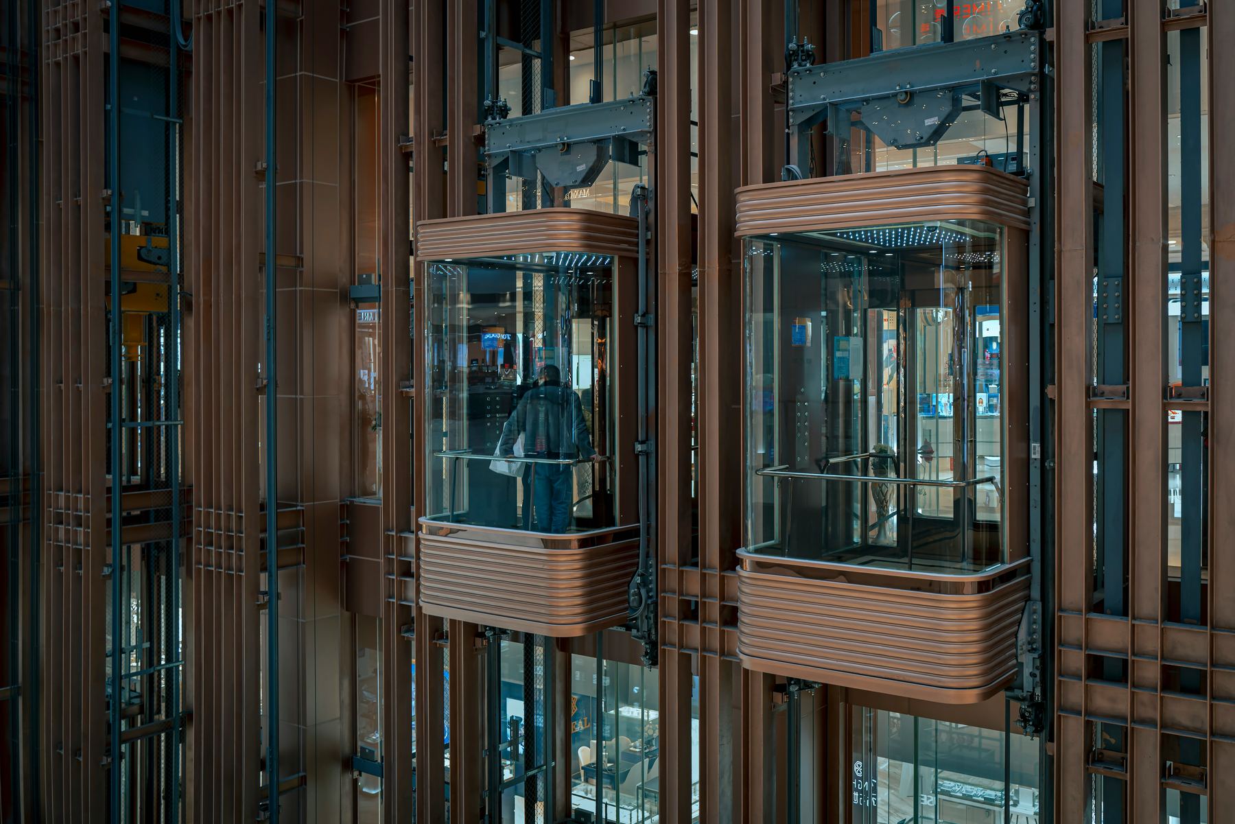 Bank of panoramic glass elevators with bronze finish in a hotel atrium, passengers visible inside