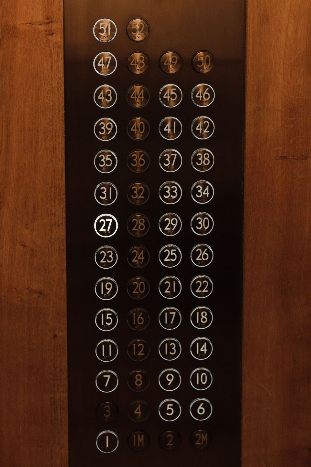 Dense elevator control panel with floor buttons for over fifty floors, warm wood and brass finish