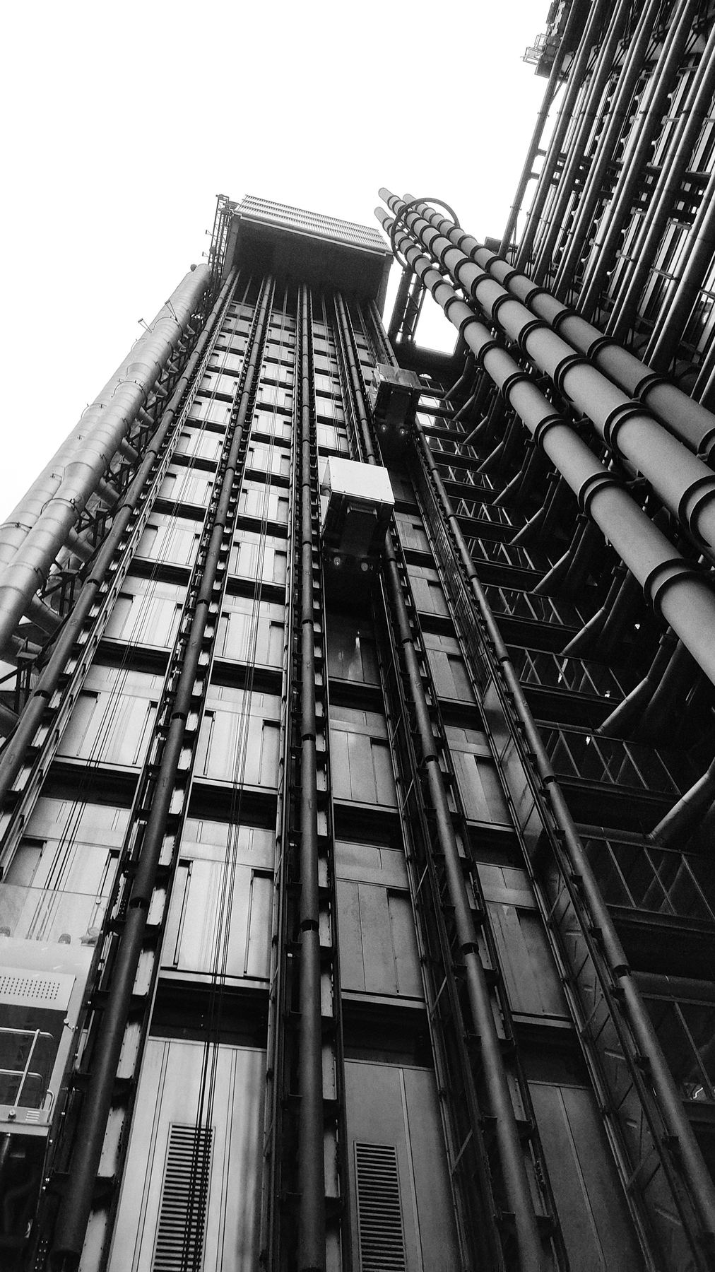 Black and white view of an exterior elevator and structural piping system on a large building