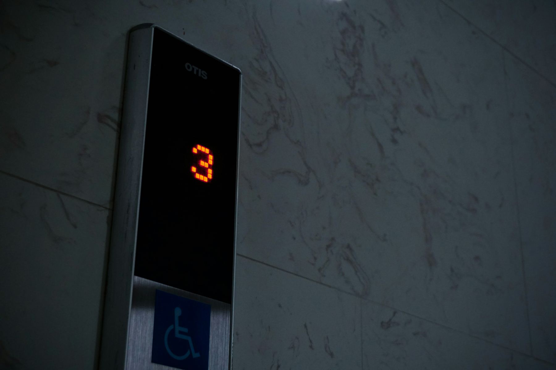 Elevator floor indicator display next to a wheelchair accessibility sign on a marble wall