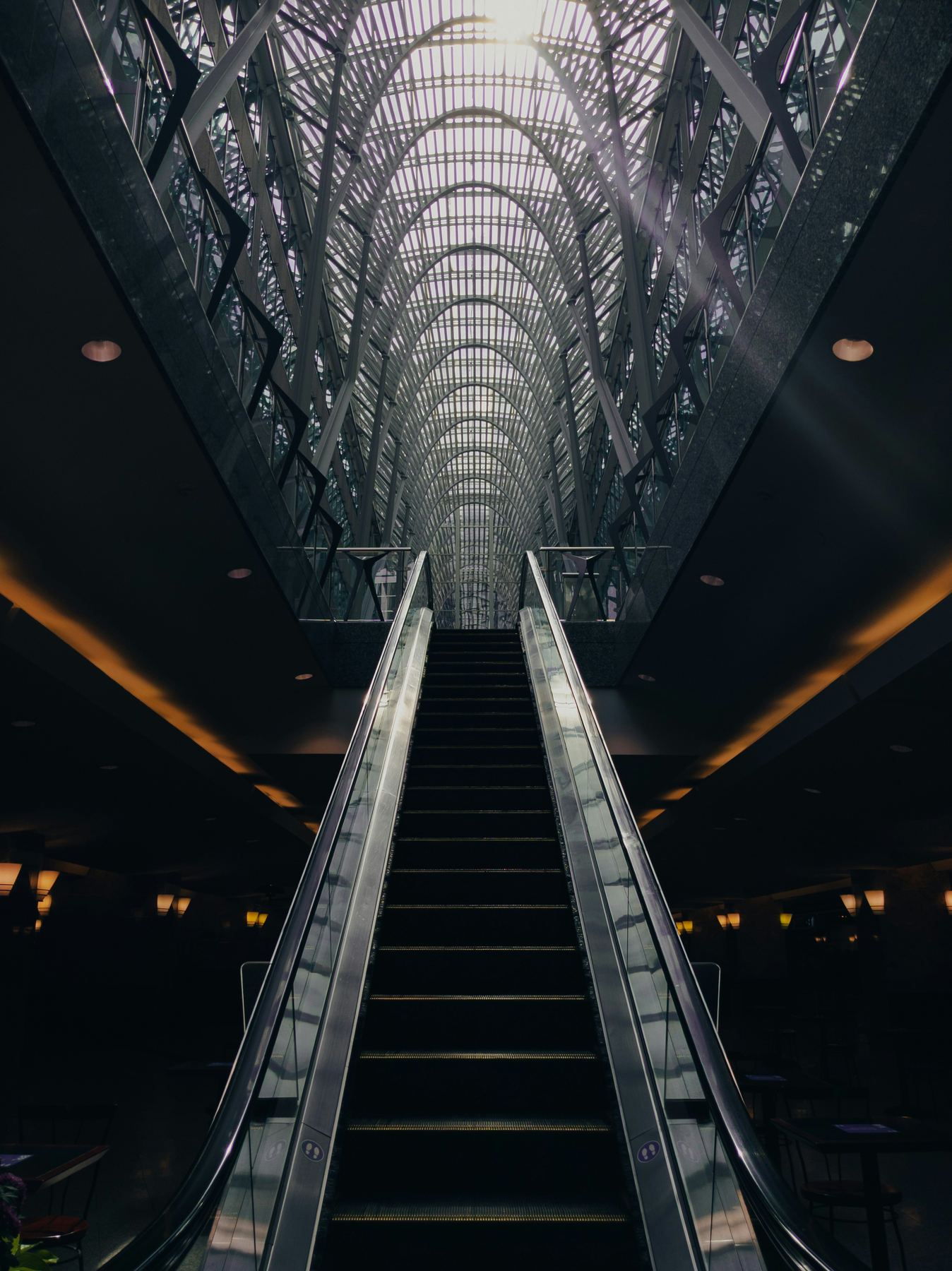 Dramatic upward view of an escalator beneath a large atrium skylight
