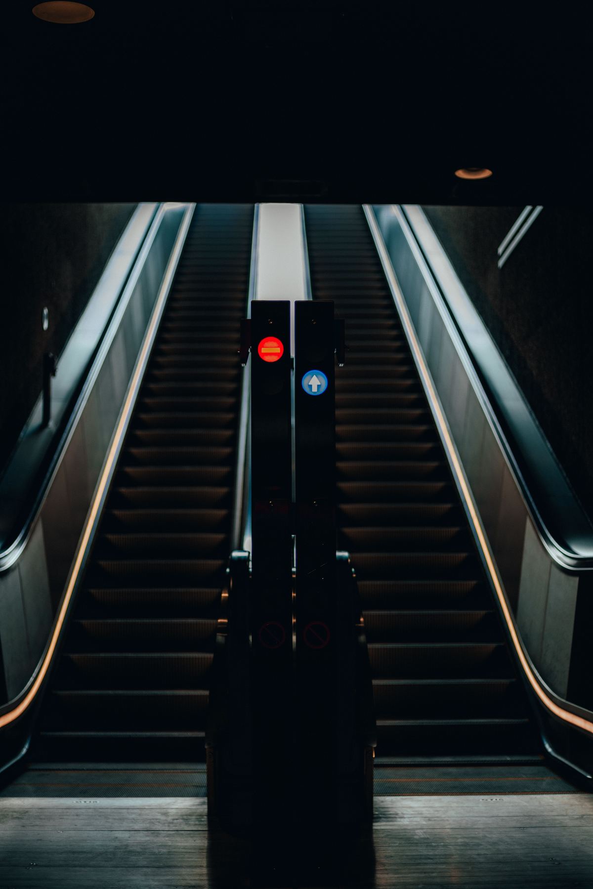 A single escalator descending into a dark passage with directional safety signage visible