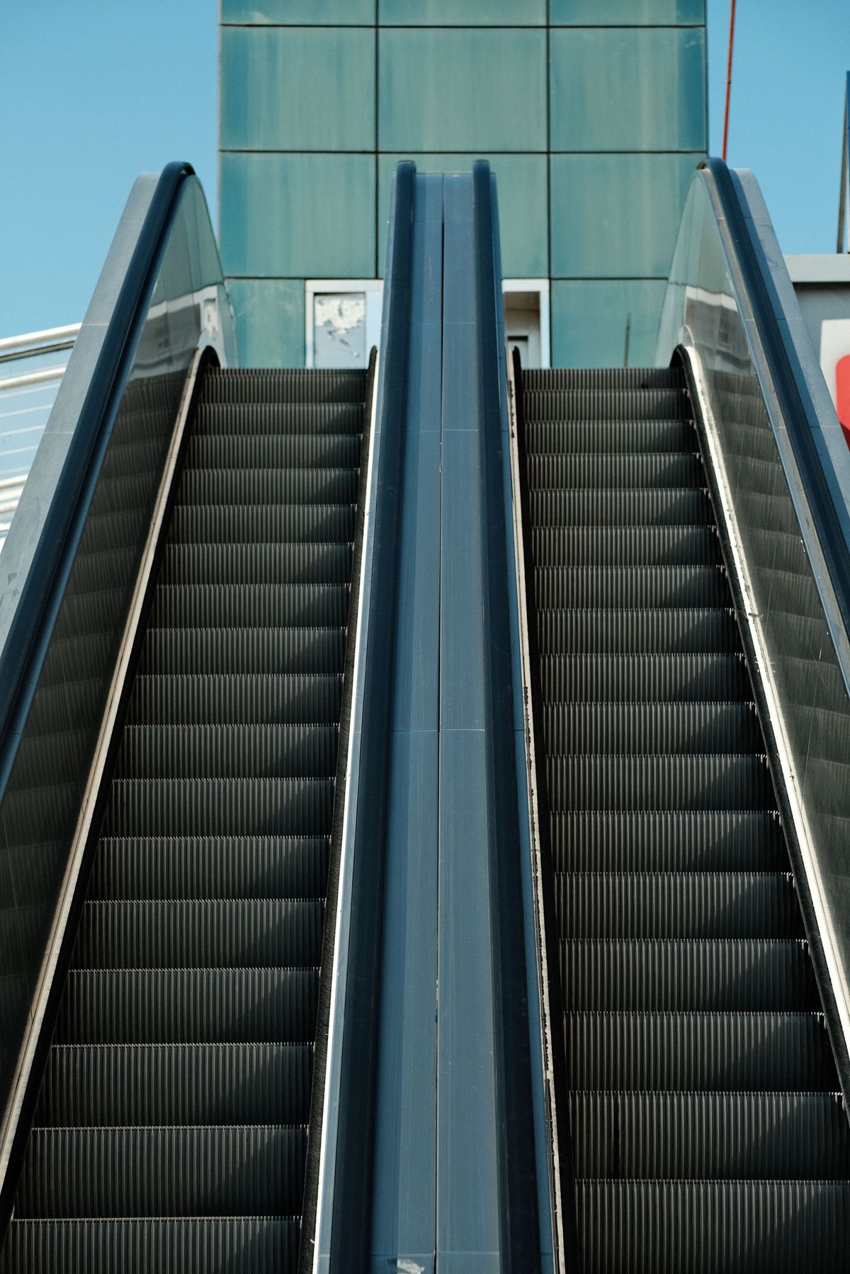 Symmetrical escalators converging toward a glass building facade in daylight