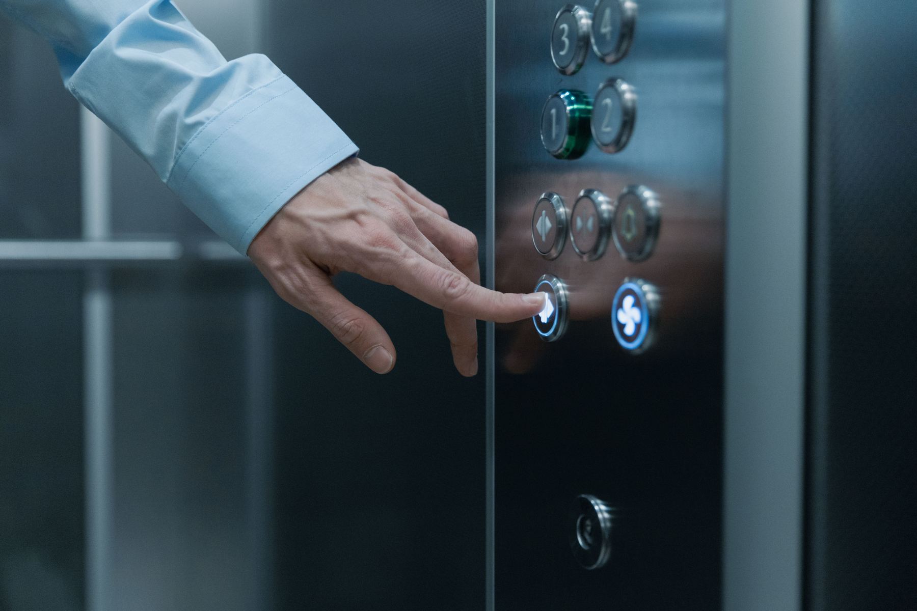 Close-up of a hand pressing an illuminated elevator call button